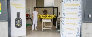 Mitarbeiter von Genusskoarl neben Firmenlogo in Betriebshalle