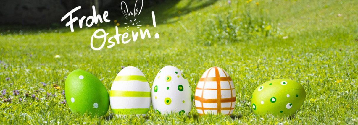 Fünf dekorierte Ostereier in Grün und Weiß stehen auf Gras in einer sonnigen Umgebung im Freien und symbolisieren Frische und Naturstrom. Frohe Ostern! mit Hasenohren steht in weißer Schrift über den Eiern.