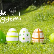 Fünf dekorierte Ostereier in Grün und Weiß stehen auf Gras in einer sonnigen Umgebung im Freien und symbolisieren Frische und Naturstrom. Frohe Ostern! mit Hasenohren steht in weißer Schrift über den Eiern.